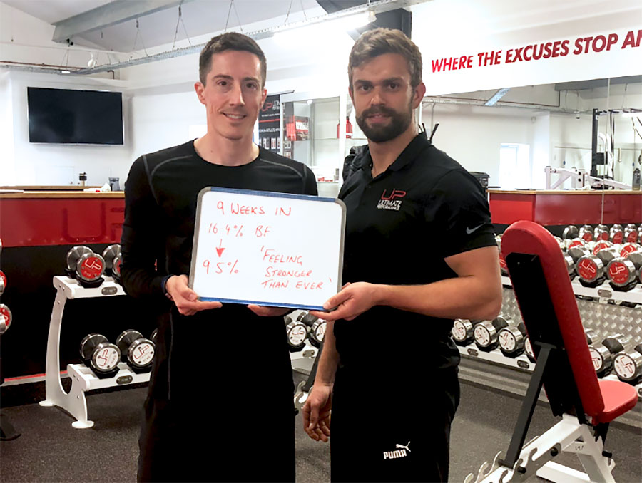 David-in-gym-with-trainer-and-sign | Ultimate Performance | Ultimate Performance